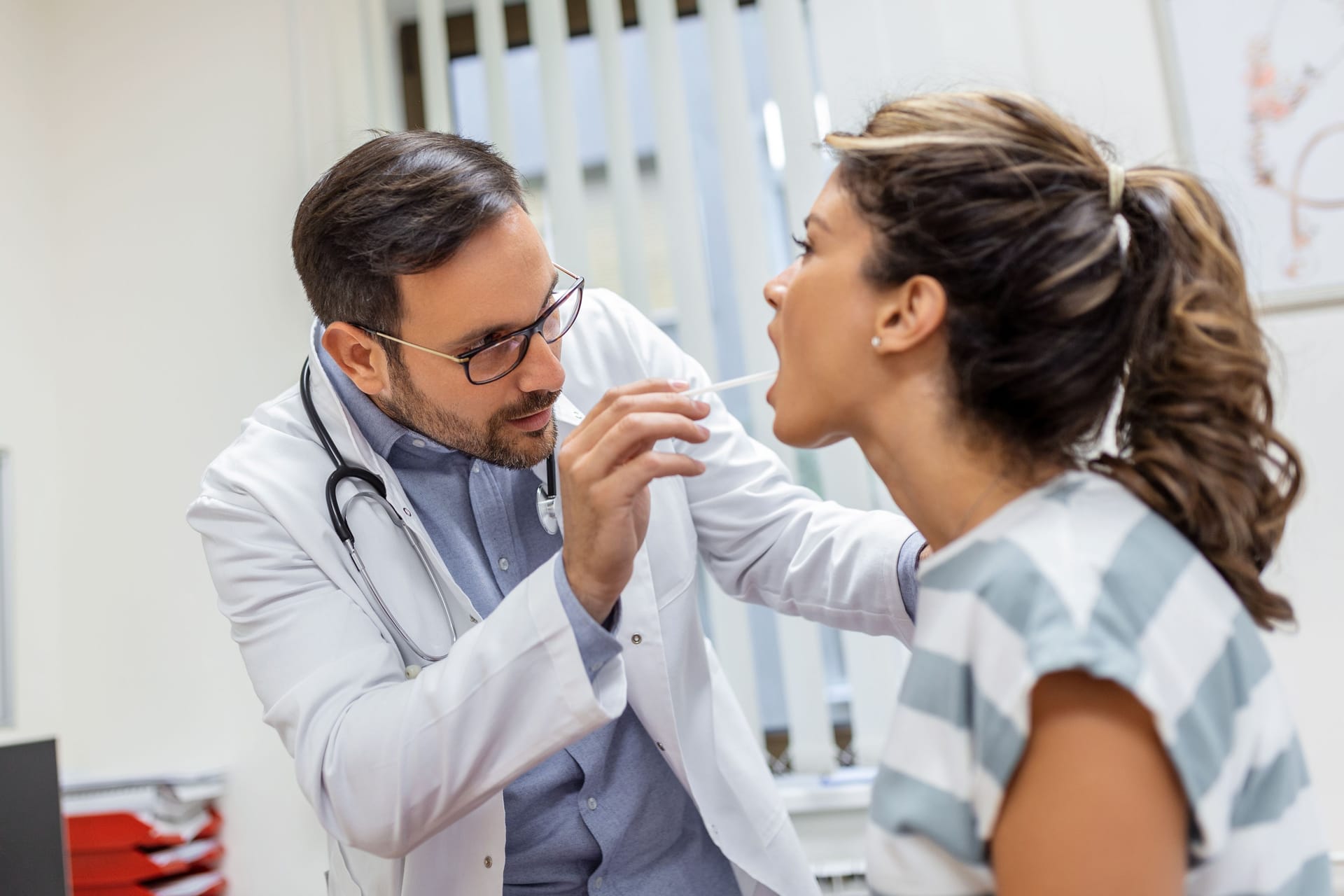 Arzt untersucht den Mundraum einer Patientin: Eine entzündete Stelle an der Zunge kann viele Ursachen haben. Arzt untersucht den Mundraum einer Patientin: Eine entzündete Stelle an der Zunge kann viele Ursachen haben.