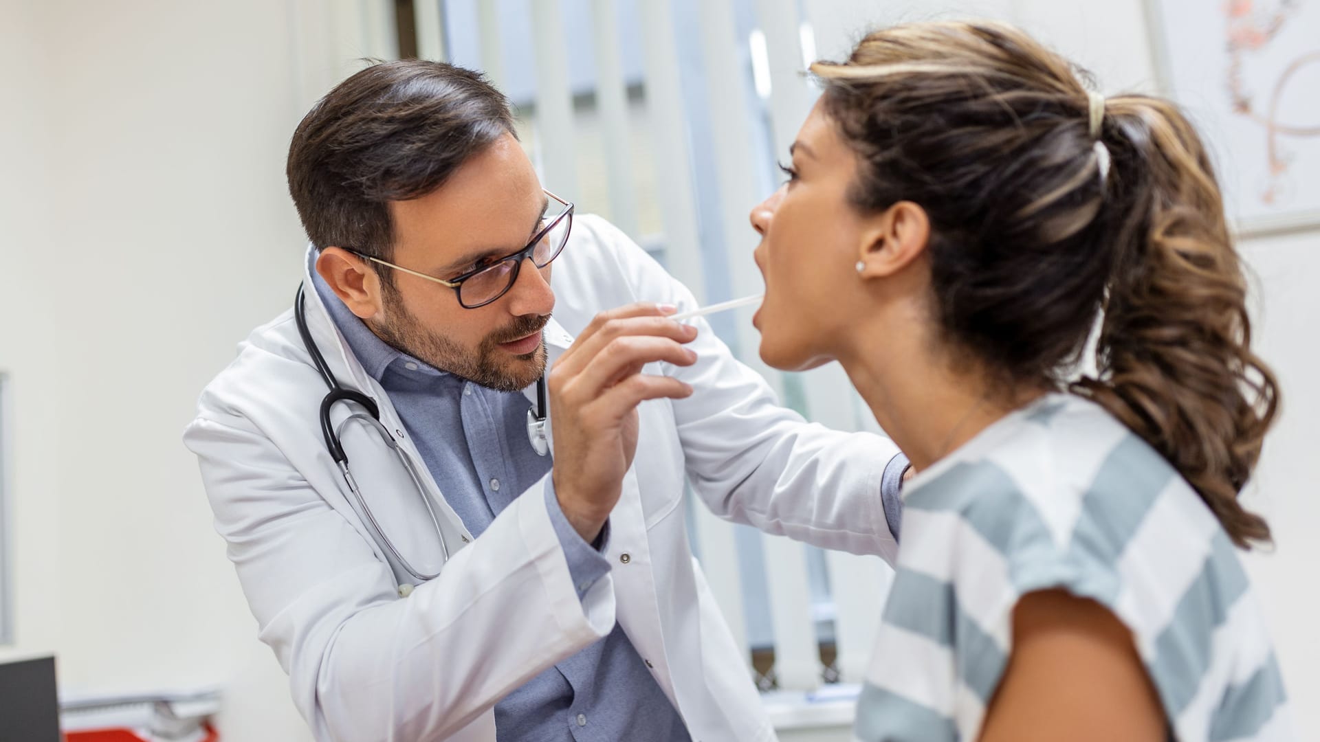 Arzt untersucht den Mundraum einer Patientin: Eine entzündete Stelle an der Zunge kann viele Ursachen haben.