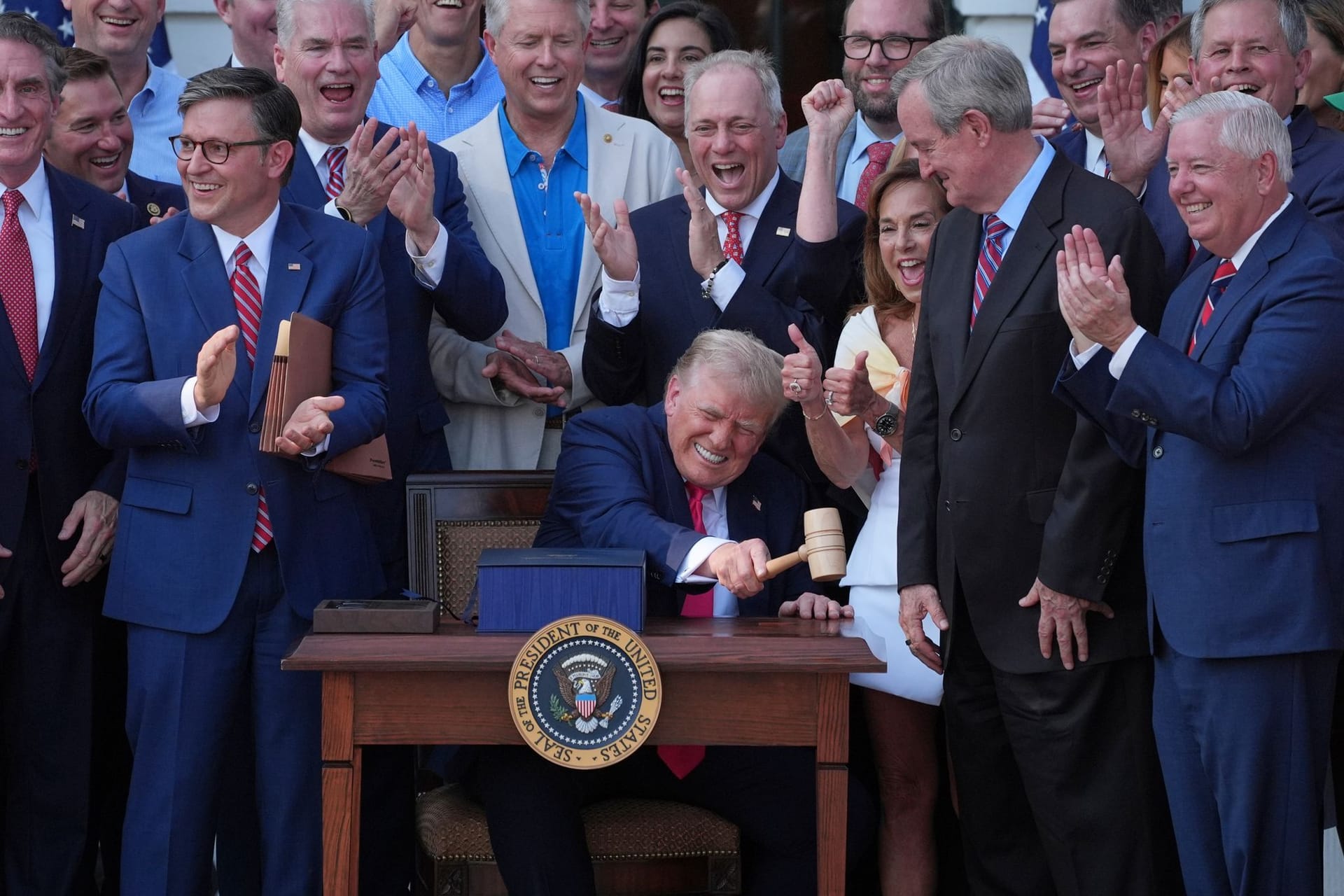 US-Präsident Donald Trump (M) schlägt mit dem Hammer, den ihm der Sprecher des Repräsentantenhauses, Mike Johnson (l), überreicht hat, nachdem er sein Gesetz über Steuererleichterungen und Ausgabenkürzungen vor dem Weißen Haus unterzeichnet hat.