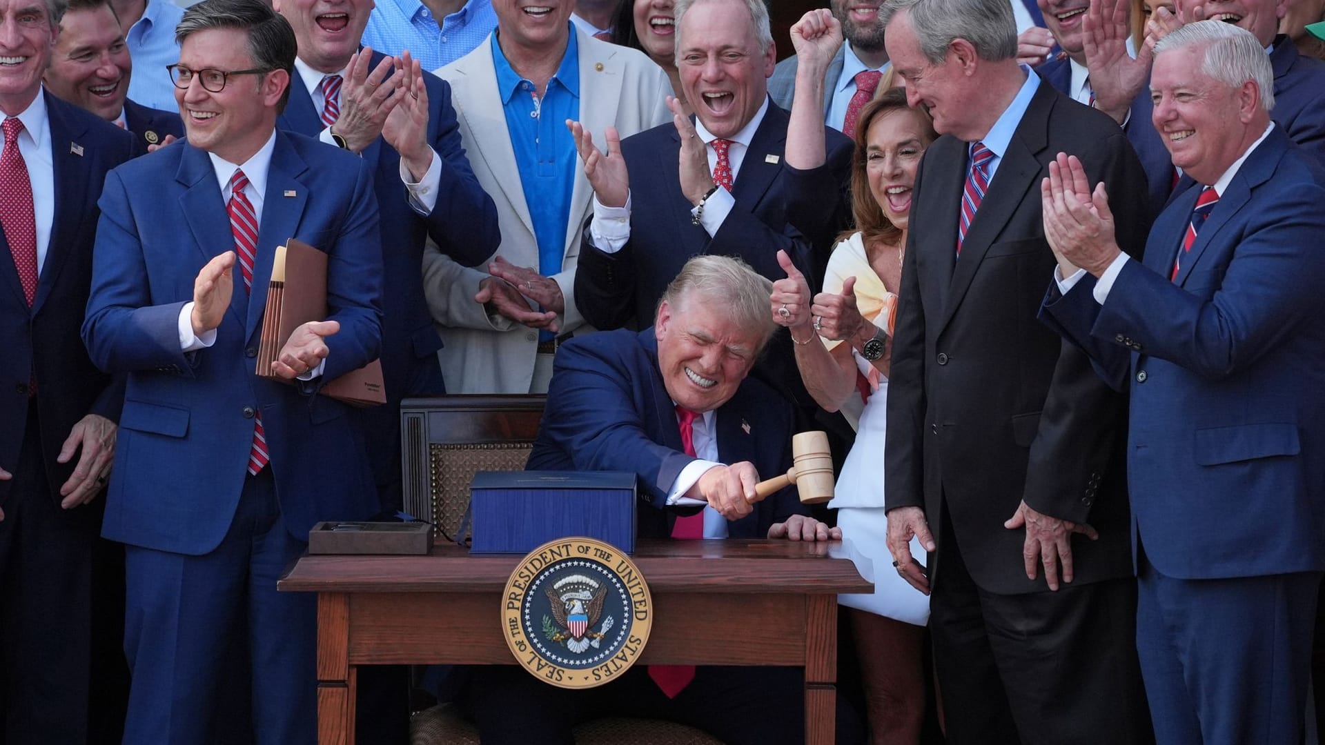 US-Präsident Donald Trump (M) schlägt mit dem Hammer, den ihm der Sprecher des Repräsentantenhauses, Mike Johnson (l), überreicht hat, nachdem er sein Gesetz über Steuererleichterungen und Ausgabenkürzungen vor dem Weißen Haus unterzeichnet hat.
