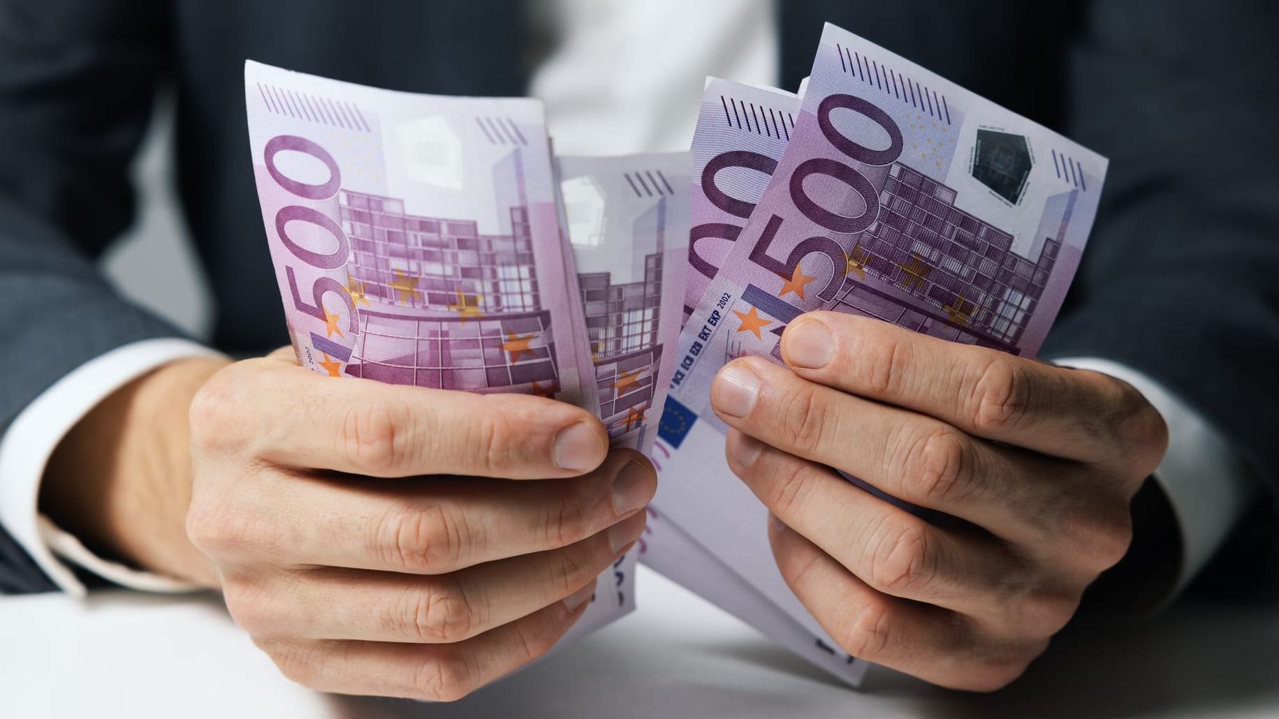 Hände halten mehrere 500-Euro-Geldscheine fest