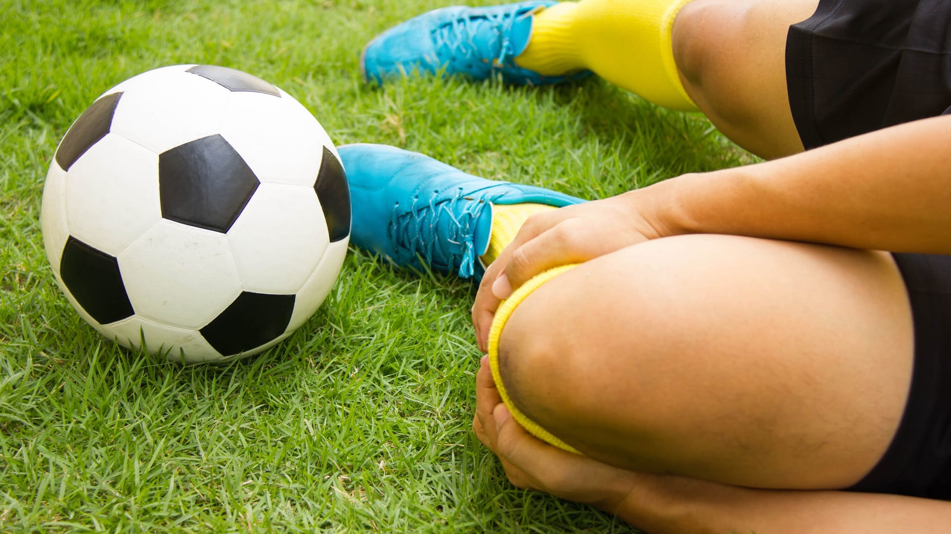 Fußballer liegt am Boden und hält sich den Unterschenkel: Ein Wadenbeinbruch entsteht häufig beim Sport.