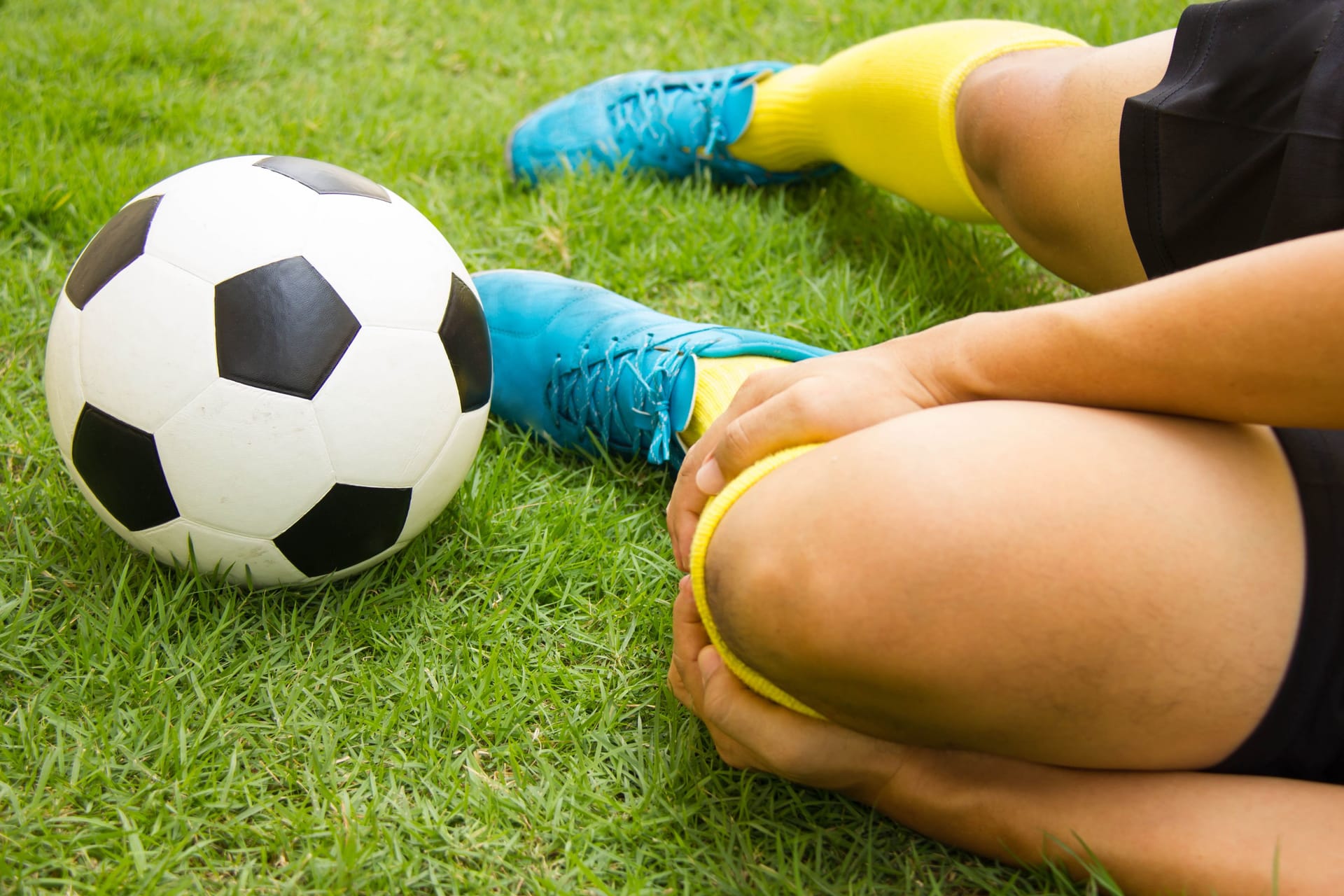 Fußballer liegt am Boden und hält sich den Unterschenkel: Ein Wadenbeinbruch entsteht häufig beim Sport.