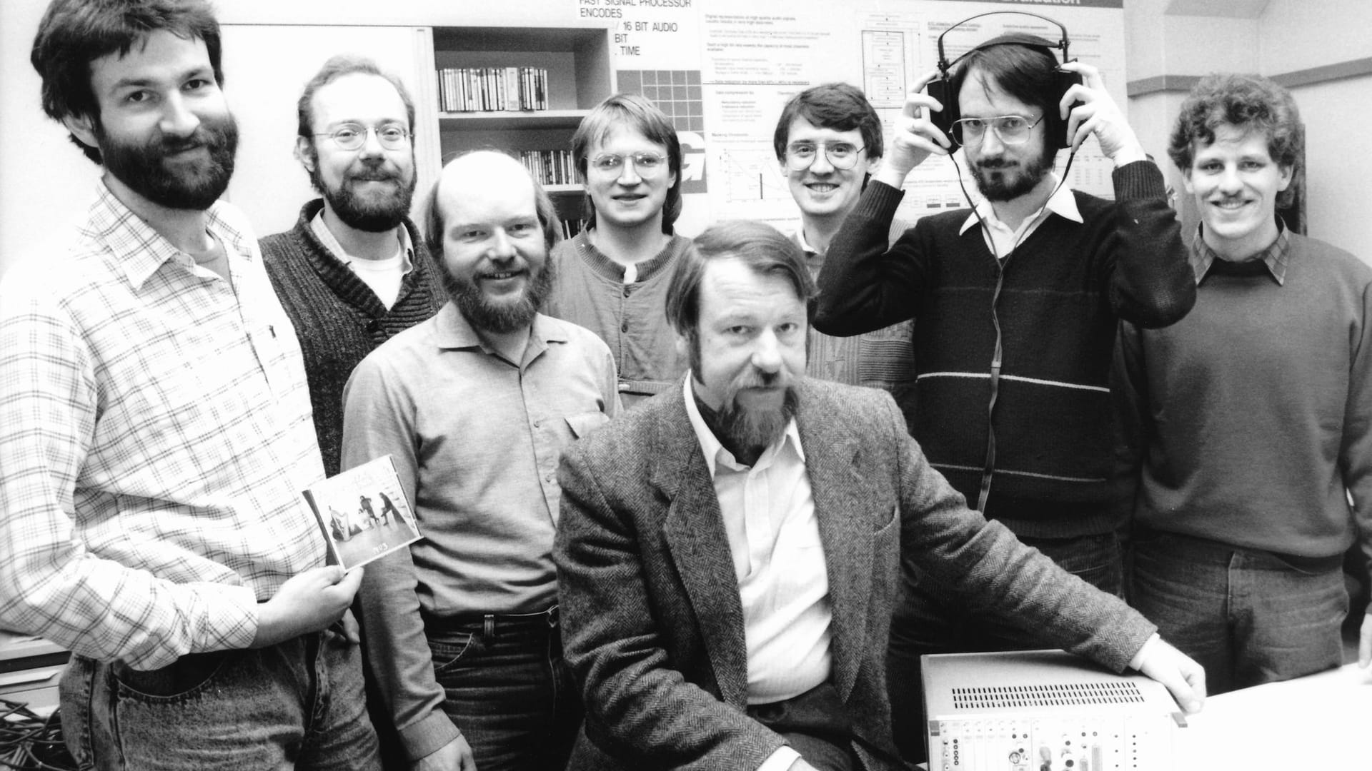 Das MP3-Team aus Erlangen um Heinz Gerhäuser (sitzend): Von Links: Harald Popp, Stefan Krägeloh, Harmut Schott, Berhard Grill, Heinz Gerhäuser, Ernst Eberlein, Karlheinz Brandenburg (mit Kopfhörer) und Thomas Sporer. Diese Aufnahme entstand 1987 am Fraunhofer-Institut für Integrierte Schaltungen IIS in Erlangen.