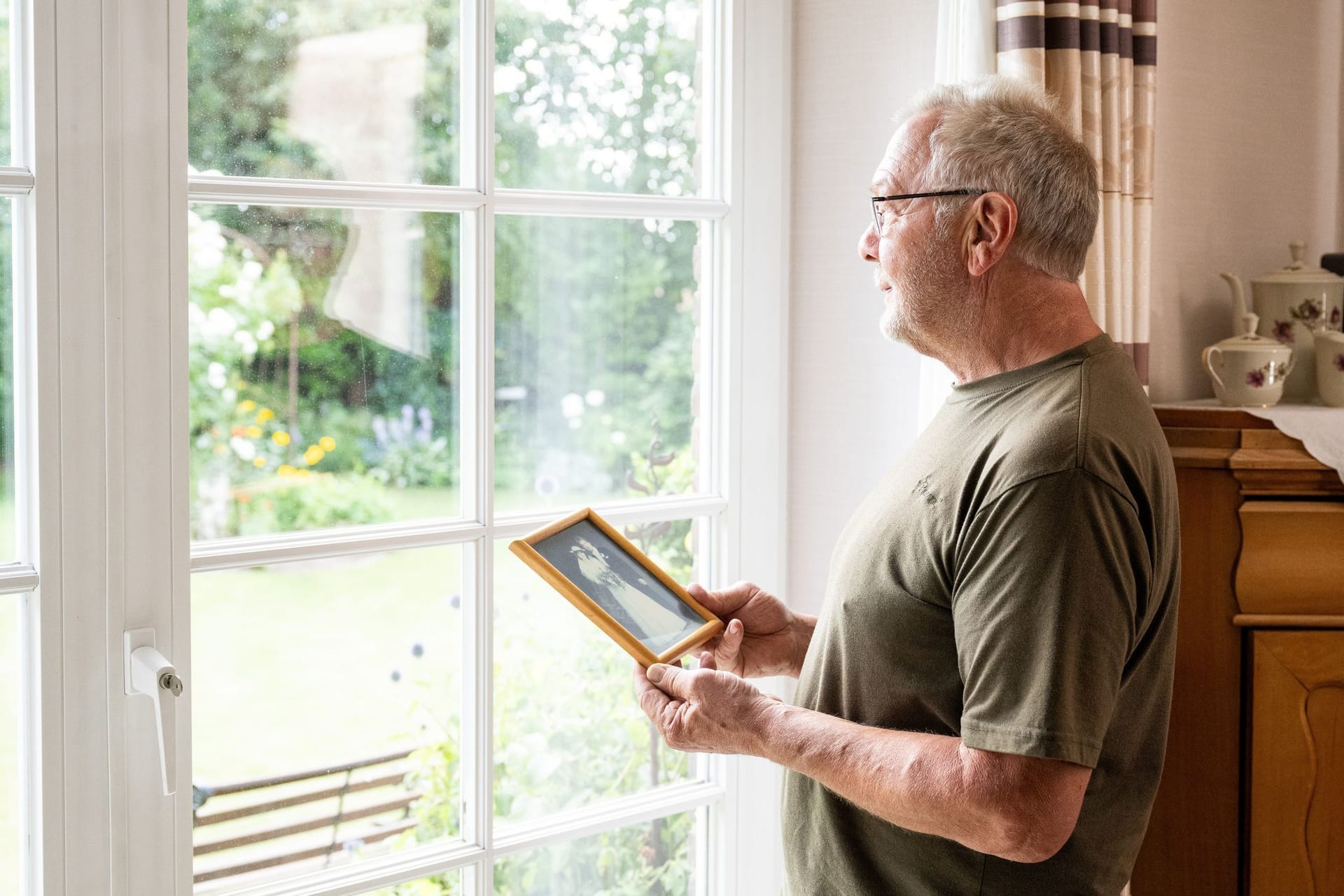 Mann steht mit einem Hochzeitsfoto am Fenster