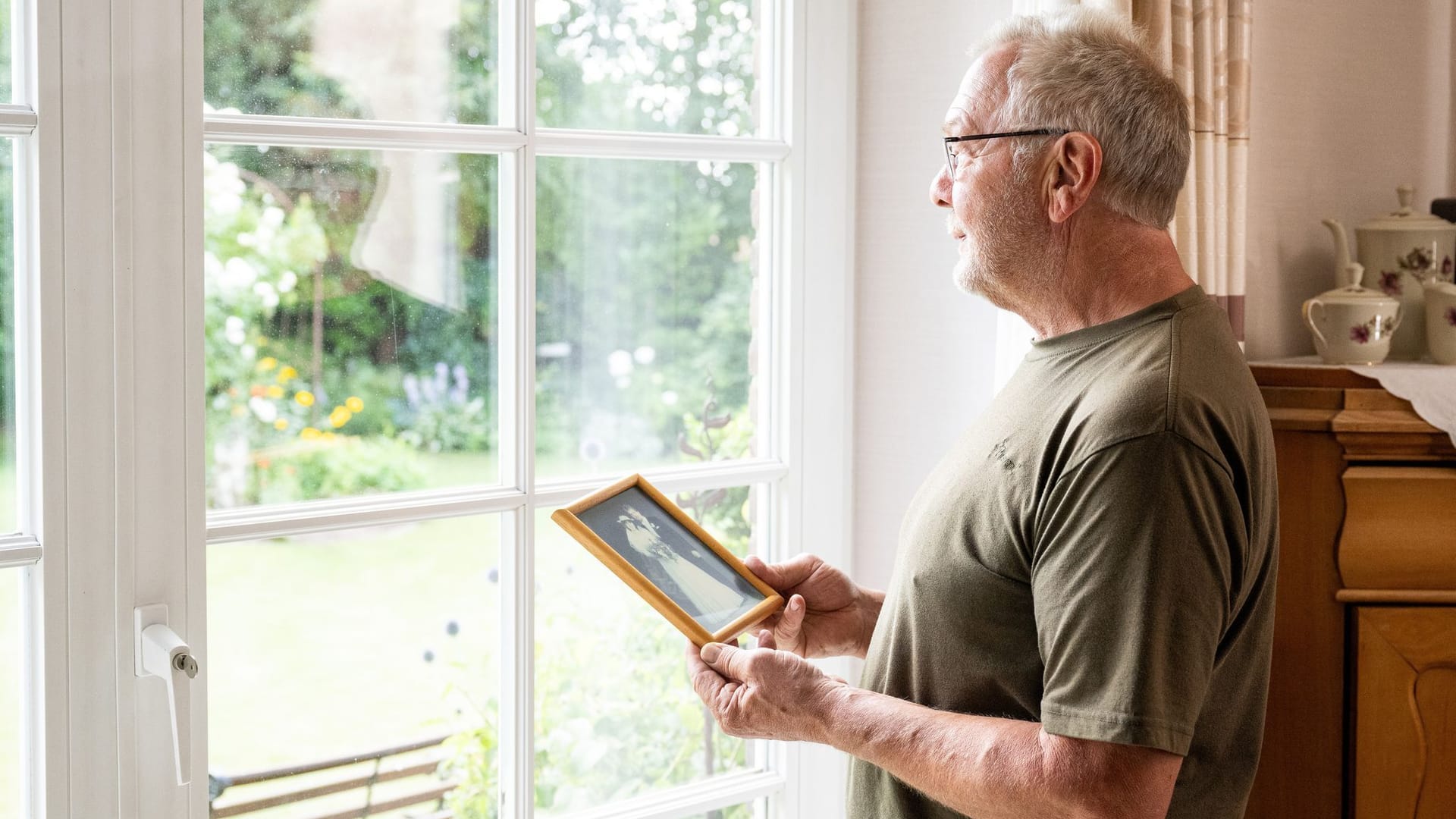 Mann steht mit einem Hochzeitsfoto am Fenster