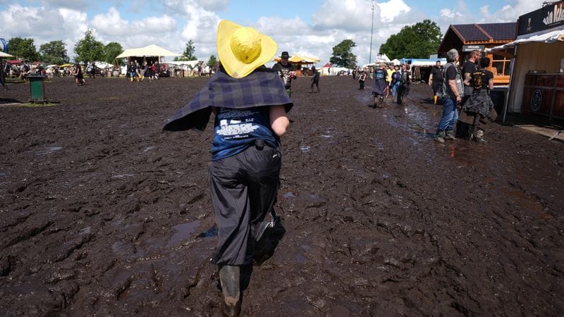 Metal-Fans gehen über das matschige Festivalgelände des Wacken Open Airs.
