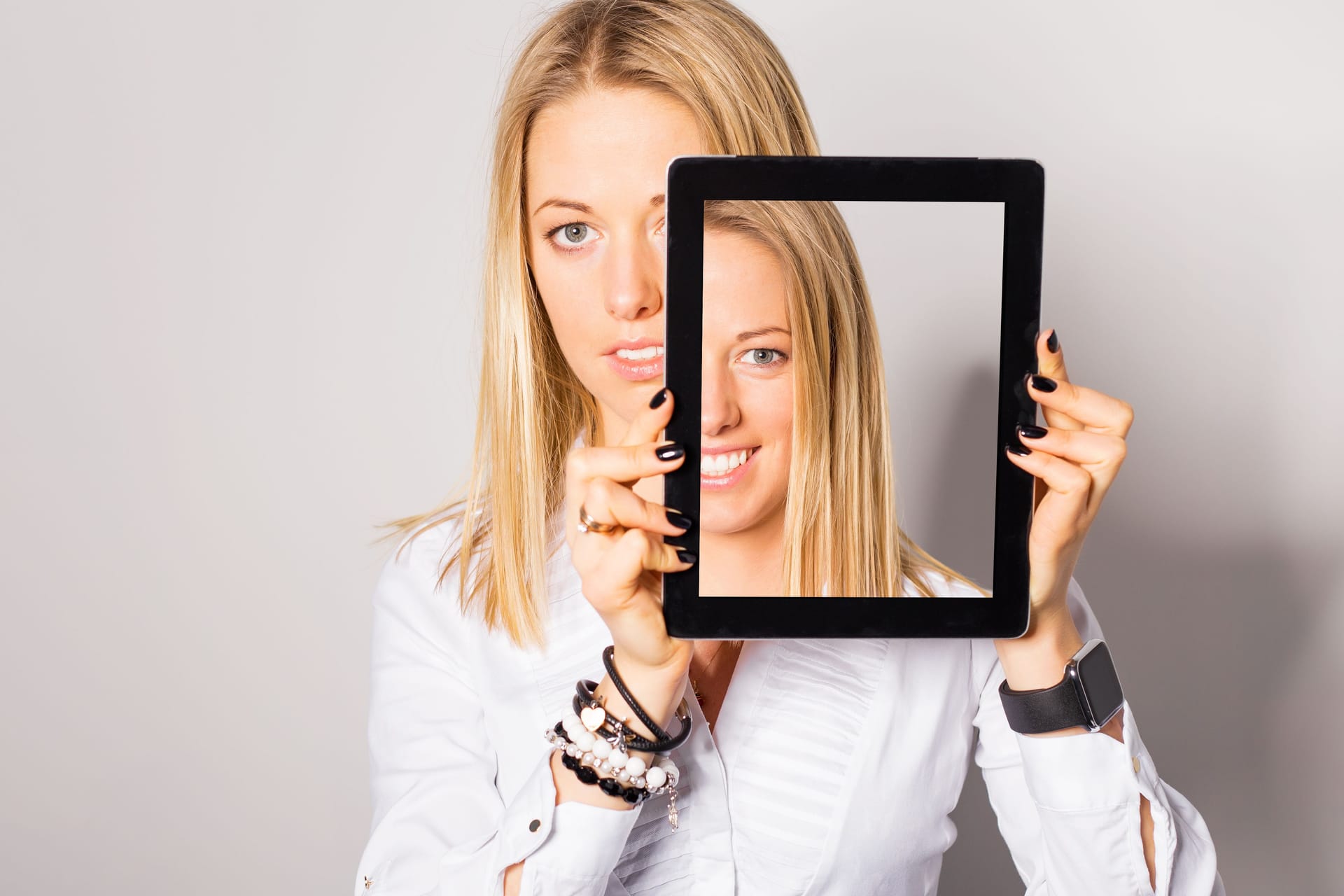 Frau hält sich Tablet vors Gesicht: Bei einer Gesichtslähmung lässt sich ein Teil der Gesichtsmuskeln nicht so wie gewohnt bewegen.