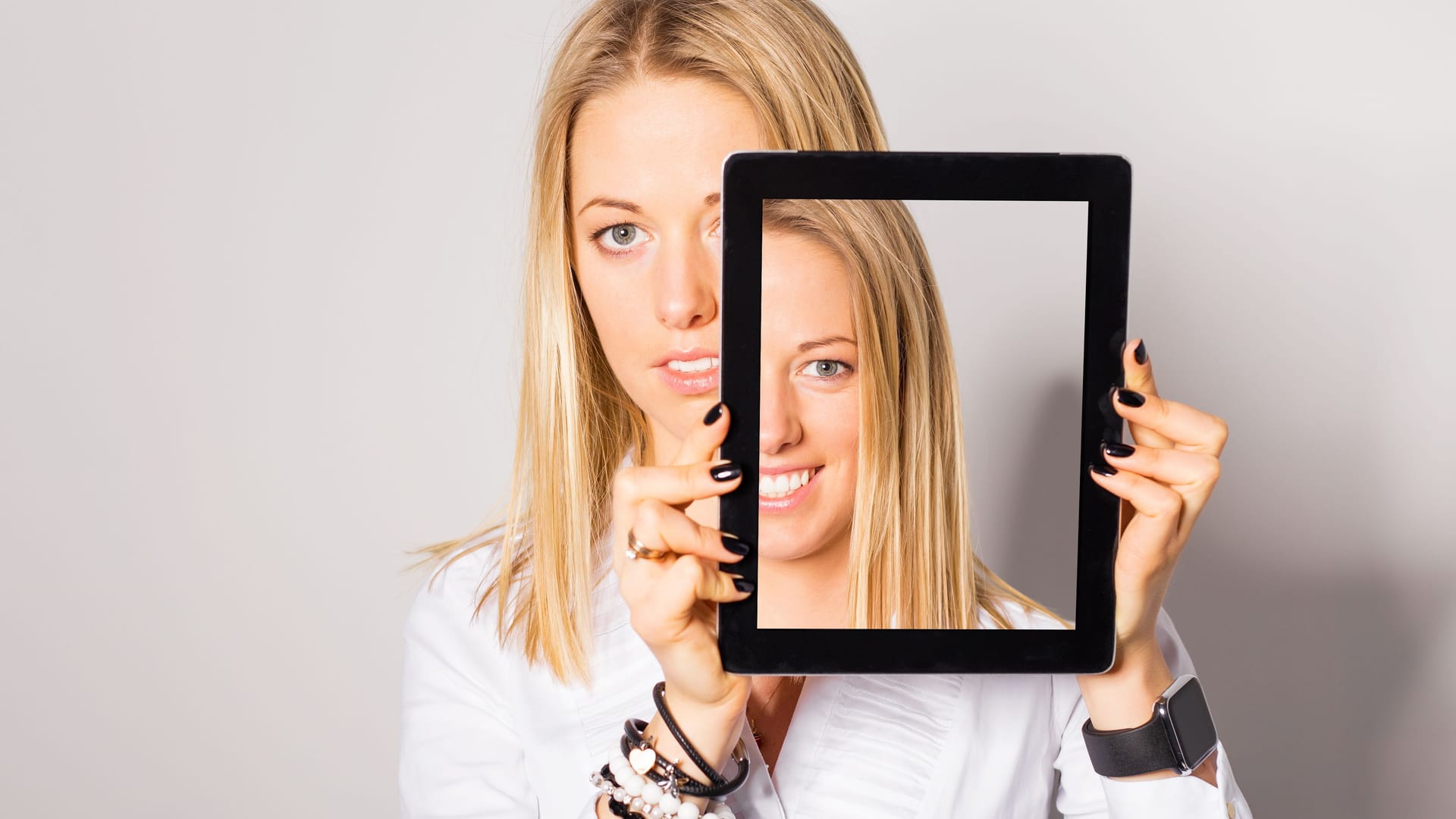 Frau hält sich Tablet vors Gesicht: Bei einer Gesichtslähmung lässt sich ein Teil der Gesichtsmuskeln nicht so wie gewohnt bewegen.