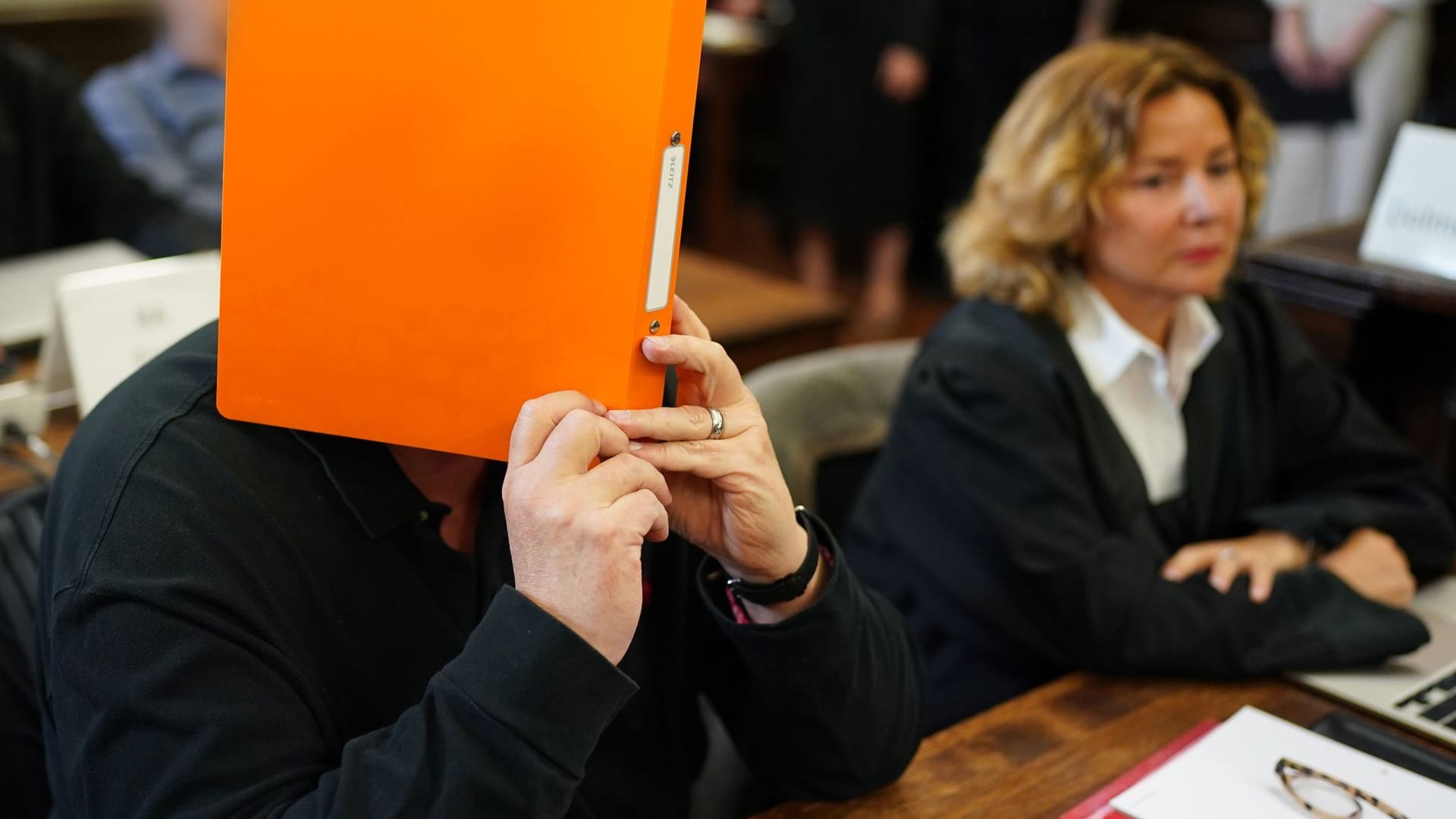 Verteidigerin Gül Pinar sitzt neben ihrem Mandanten Andreas Persihl: Er versteckt sich hinter einem orangefarbenen Ordner.