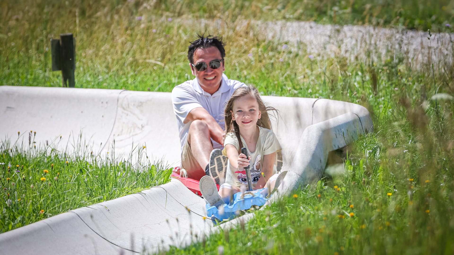 Vater und Tochter fahren eine Sommerrodelbahn hinab.