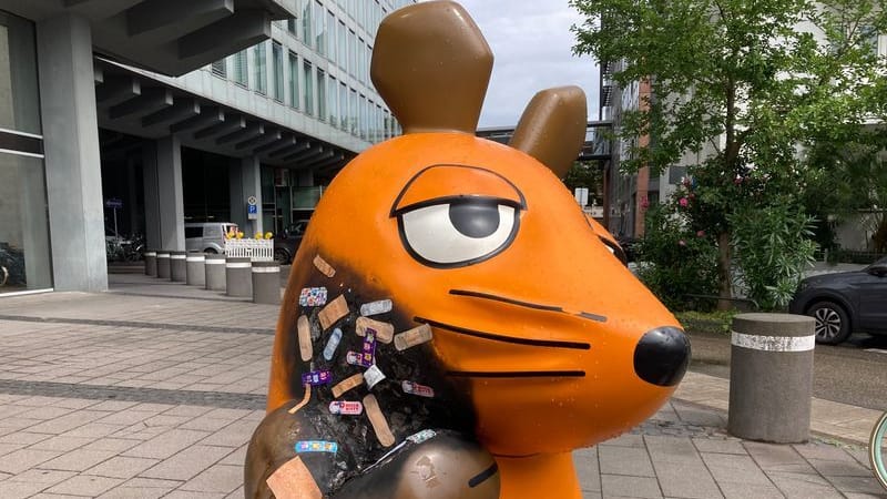 Nach einem mutmaßlichen Brandanschlag auf die Maus-Figur vor dem WDR-Gebäude in Köln sind mehrere Pflaster auf der verbrannten Stelle zu sehen.