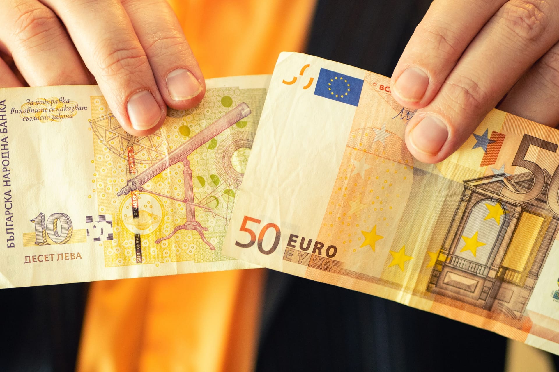Ein Mann hält einen 10-Lewa-Schein (l.) und eine 50-Euro-Münze in die Kamera: Die Bulgaren sollen ab 2026 zur Euro-Zone gehören. Ein Mann hält einen 10-Lewa-Schein (l.) und eine 50-Euro-Münze in die Kamera: Die Bulgaren sollen ab 2026 zur Euro-Zone gehören.
