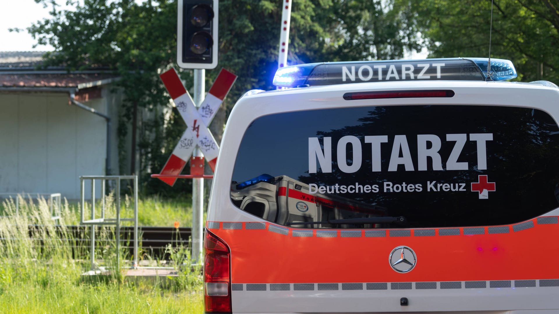 Ein Einsatzfahrzeug vom Deutschen Roten Kreuz steht mit Blaulicht bei einem Bahnunfall (Symbolbild): Ein Auto ist auf den Bahnübergang gefahren und mit einem Zug kollidiert.