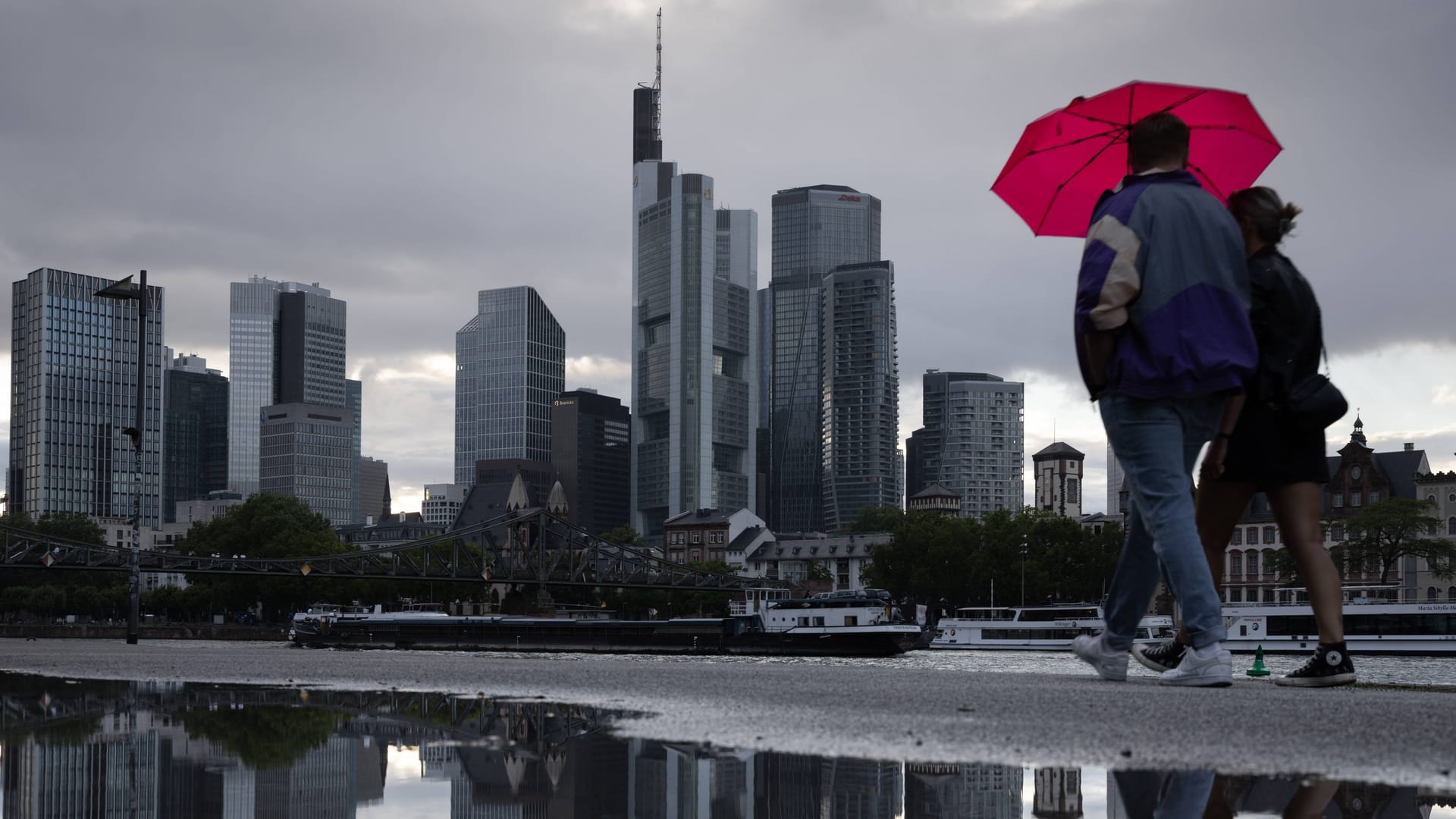 Zwei Personen spazieren mit einem Regenschirm vor der Frankfurter Skyline (Archivbild):