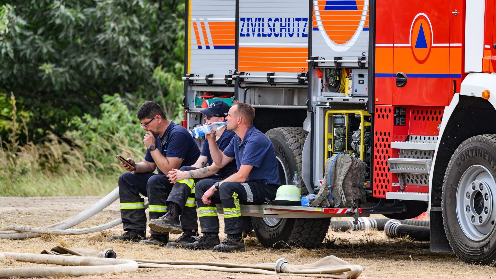 Feuerwehrleute im Waldbrand in der Gohrischheide sitzen auf einer Feuerwehr und machen eine Pause: Die Lage vor Ort hat sich stabilisiert – Katastrophenalarm wurde inzwischen aufgehoben.