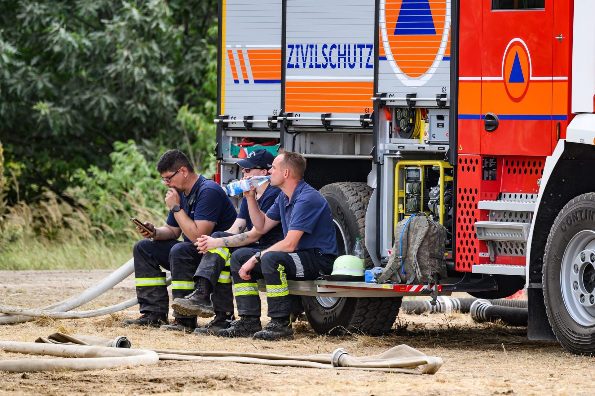 Feuerwehrleute im Waldbrand in der Gohrischheide sitzen auf einer Feuerwehr und machen eine Pause: Die Lage vor Ort hat sich stabilisiert – Katastrophenalarm wurde inzwischen aufgehoben.