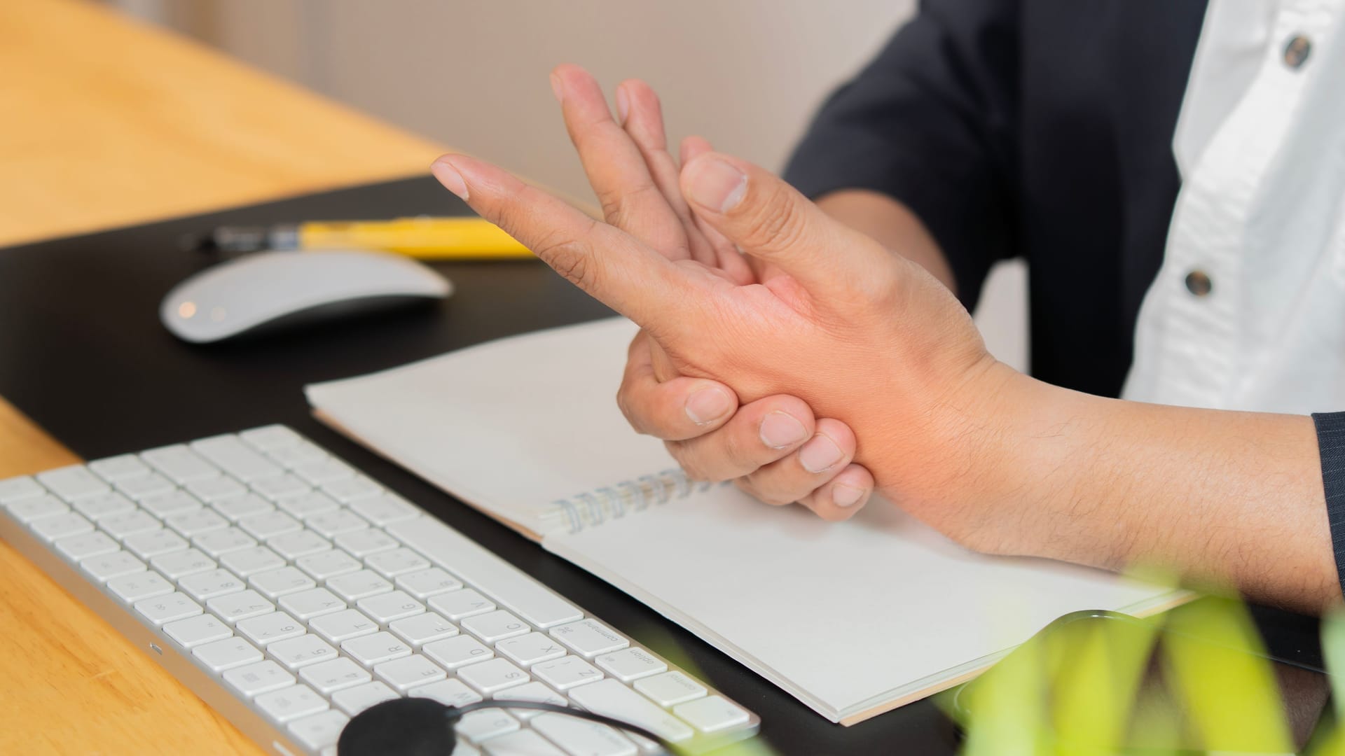 Person sitzt am Schreibtisch und hat Schmerzen in der Hand: Gelenkschmerzen können einen oder mehrere Finger betreffen. Person sitzt am Schreibtisch und hat Schmerzen in der Hand: Gelenkschmerzen können einen oder mehrere Finger betreffen.