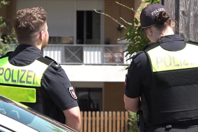 Zwei Polizisten stehen vor einem Haus (Archivbild): Die Polizei nahm den Verdächtigen in einer Wohnung des Mehrfamilienhauses fest.