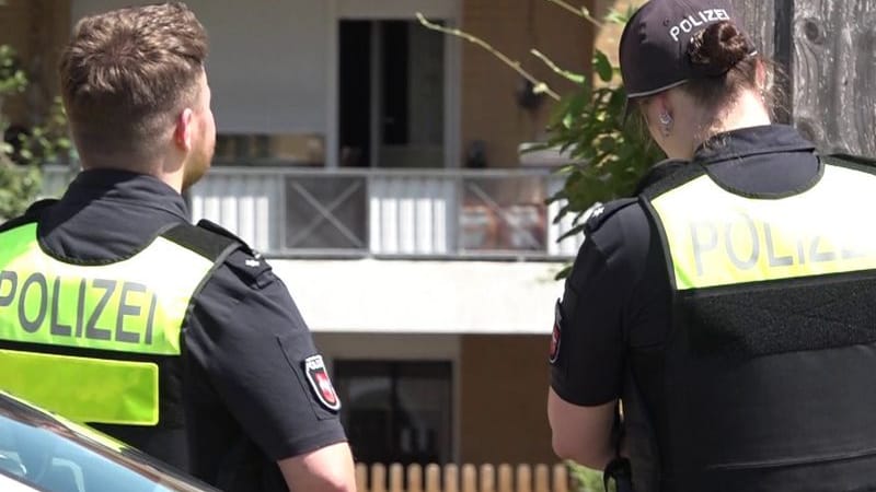Zwei Polizisten stehen vor einem Haus (Archivbild): Die Polizei nahm den Verdächtigen in einer Wohnung des Mehrfamilienhauses fest.