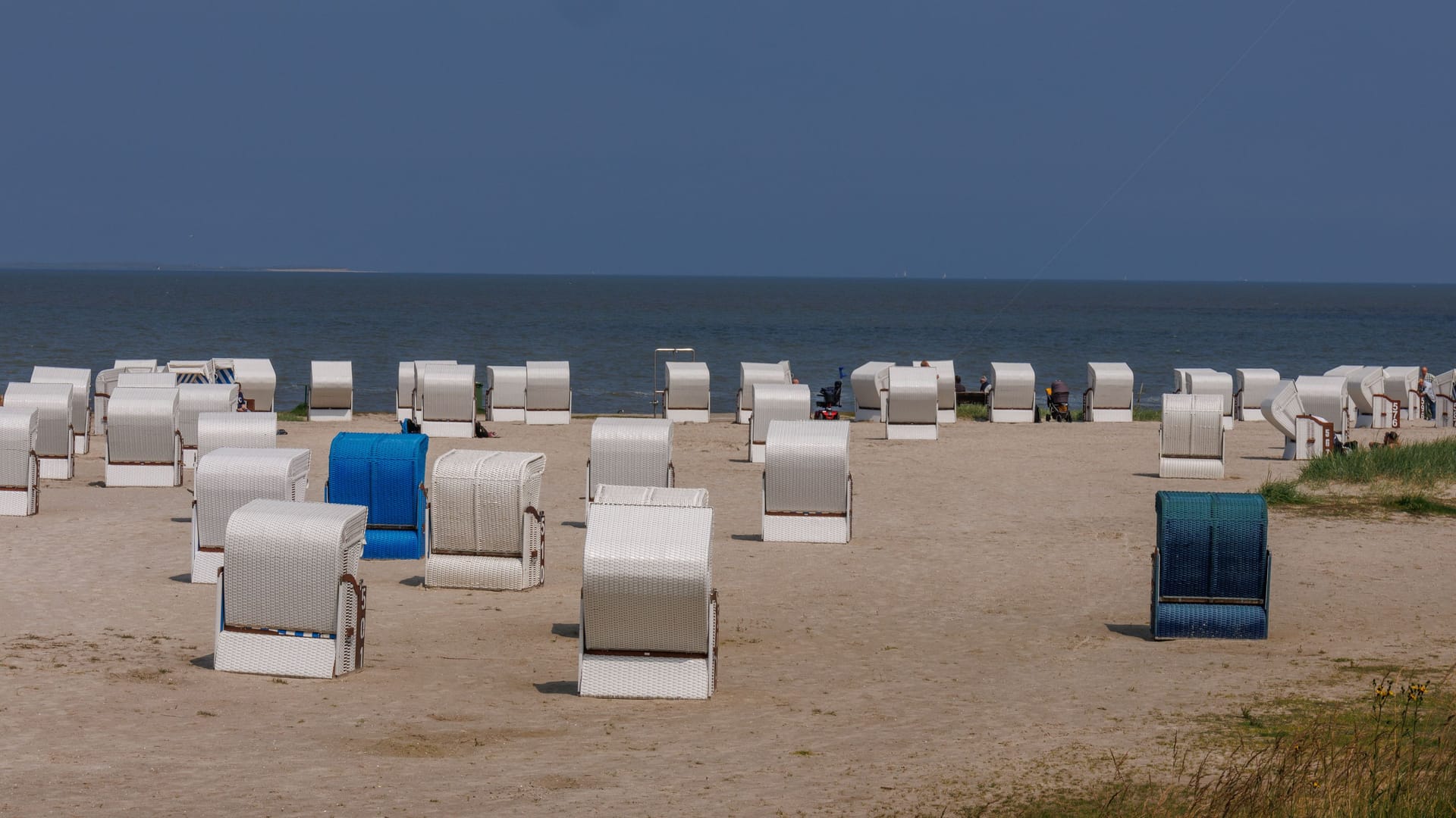 Beach chairs on a sandy shore with a calm sea and clear blue sky in the background