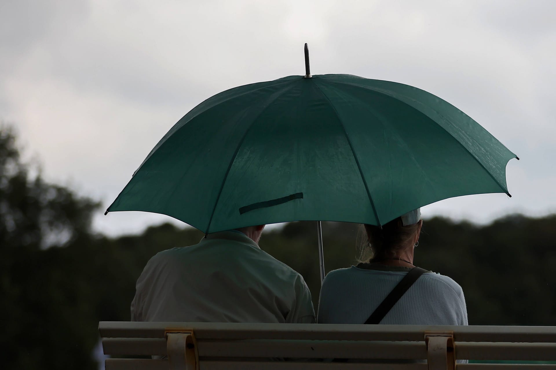 Ein Paar sitzt bei Regen mit Regenschirm auf einer Bank (Symbolbild): Sonne, Regen und Gewitter werden in Niedersachsen erwartet.