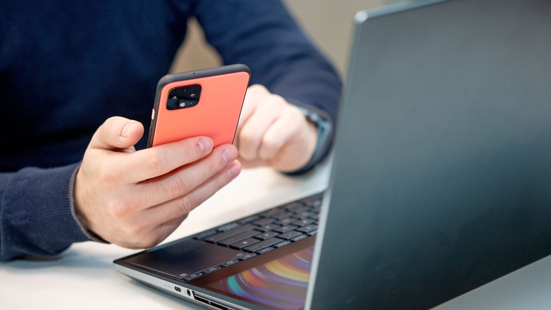Ein Mann nutzt ein Handy am Laptop Ein Mann nutzt ein Handy am Laptop