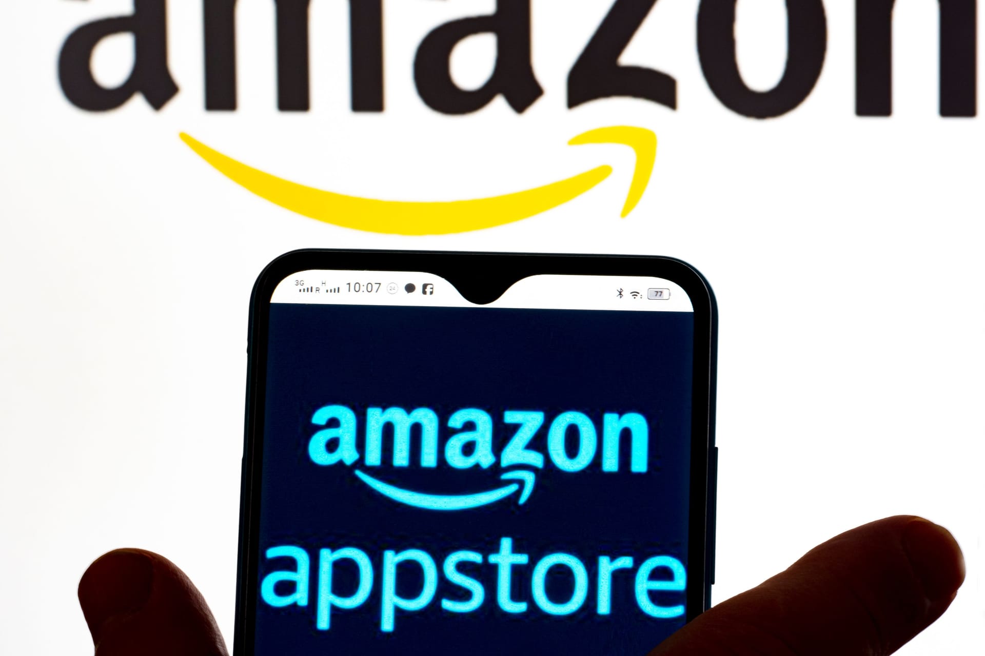 In this photo illustration, the Amazon AppStore logo is seen displayed on a smartphone screen and Amazon logo in the background.