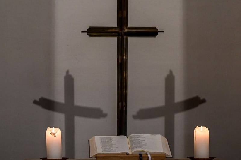 Kerzen, eine Bibel, ein Kreuz und die Schatten des Kreuzes sind in einer Kapelle zu sehen (Archivbild): Seit 2018 summieren sich die Entschädigungszahlungen auf rund eine Million Euro.