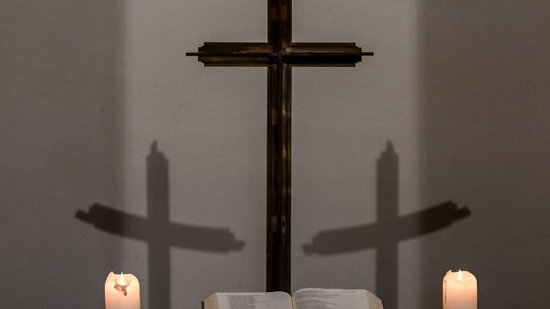 Kerzen, eine Bibel, ein Kreuz und die Schatten des Kreuzes sind in einer Kapelle zu sehen (Archivbild): Seit 2018 summieren sich die Entschädigungszahlungen auf rund eine Million Euro.