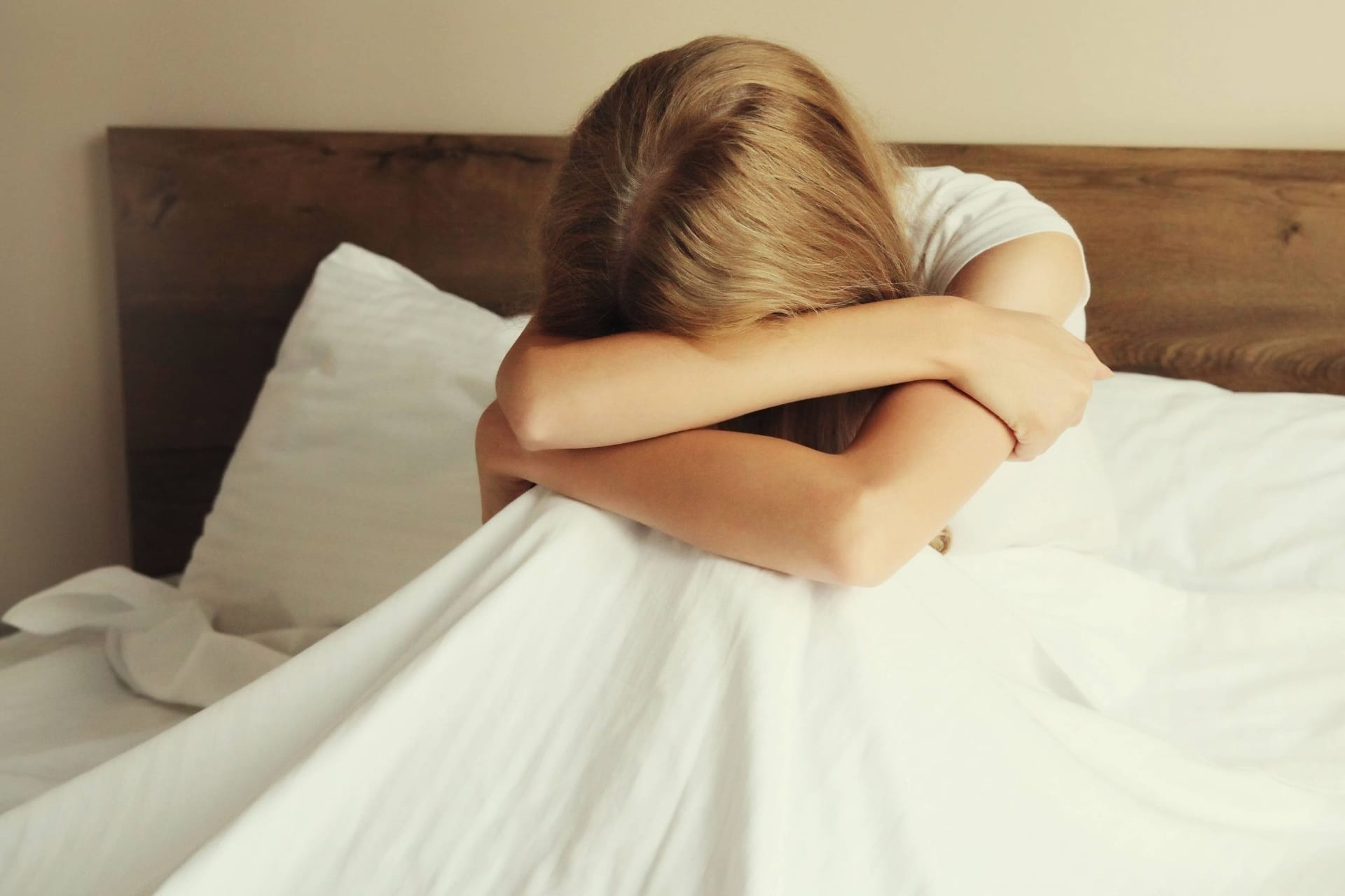 Eine aufgewühlte, weinende Frau sitzt im Bett (Symbolbild): Das Mietrecht macht es Opfern häuslicher Gewalt oft schwer, sich von den Tätern zu trennen.