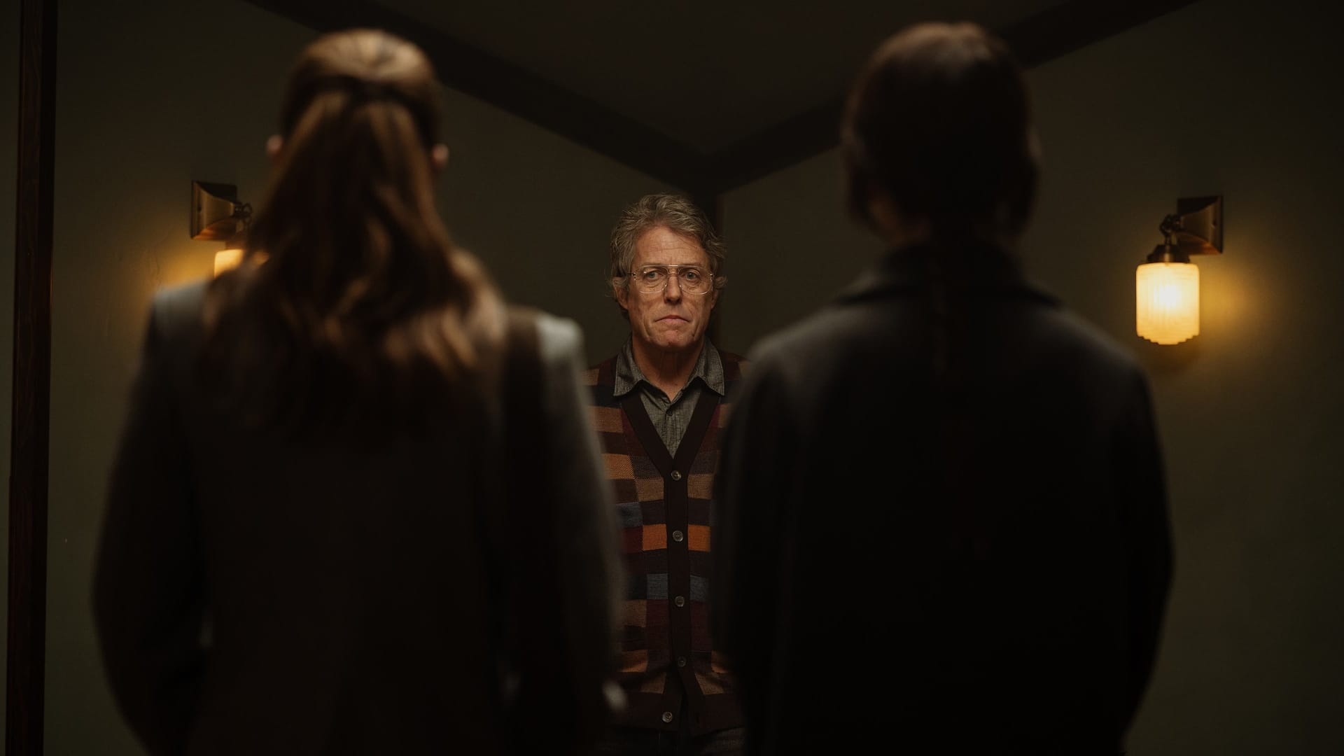 Auf dem Bild ist Schauspieler Húgh Grant in einer Szene aus dem Horrorfilm "Heretic" zu sehen. Zwei Frauen blicken ihn an und stehen mit dem Rücken zum Zuschauer.