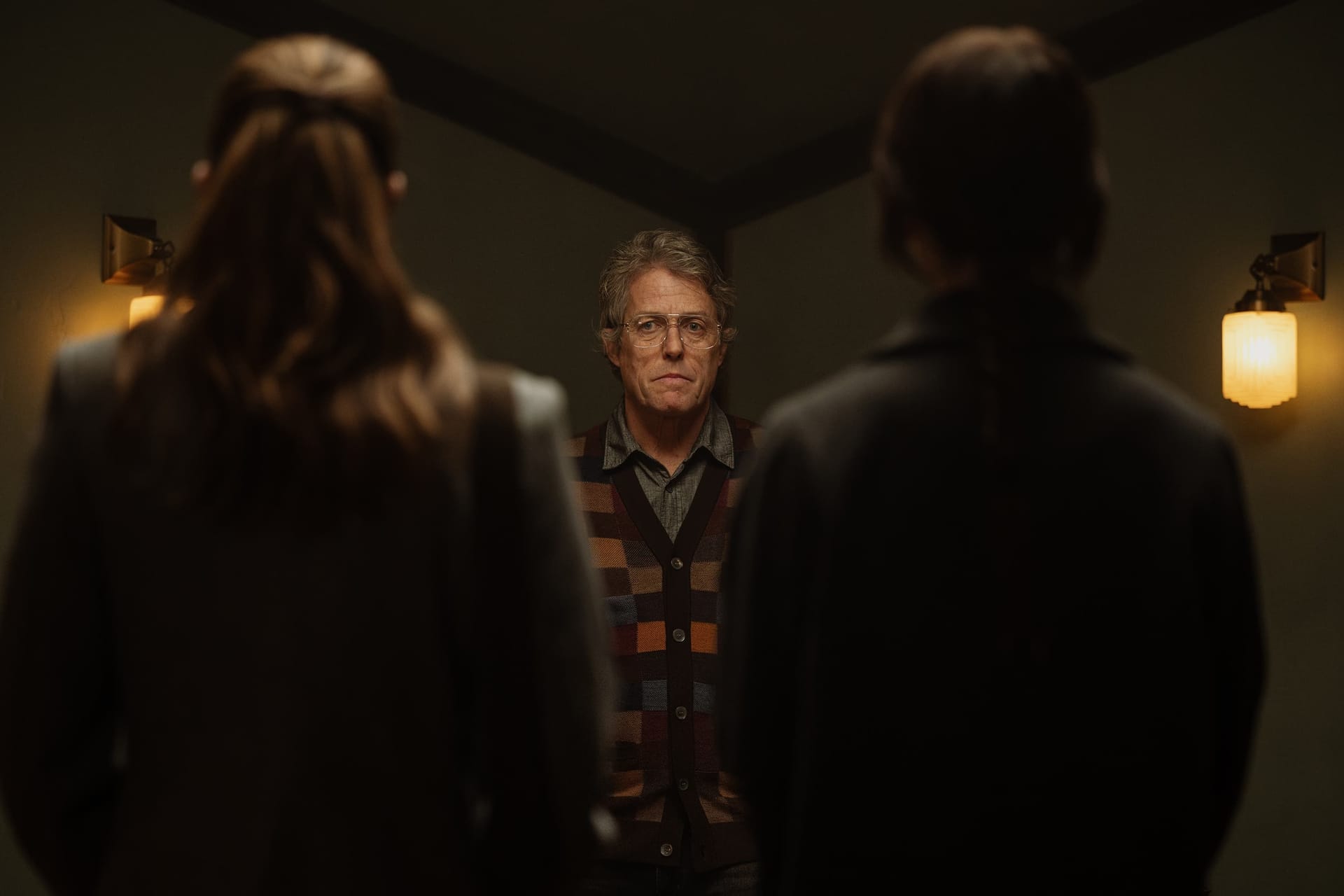 Auf dem Bild ist Schauspieler Húgh Grant in einer Szene aus dem Horrorfilm "Heretic" zu sehen. Zwei Frauen blicken ihn an und stehen mit dem Rücken zum Zuschauer.