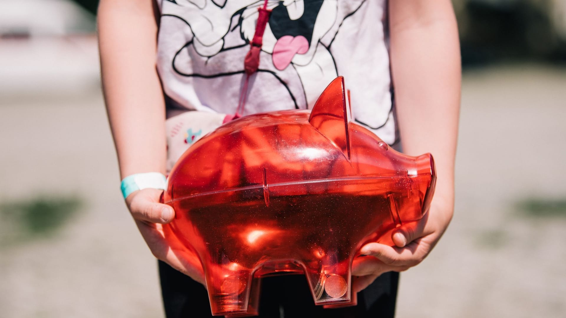 Ein Kind trägt ein rotes Sparschwein