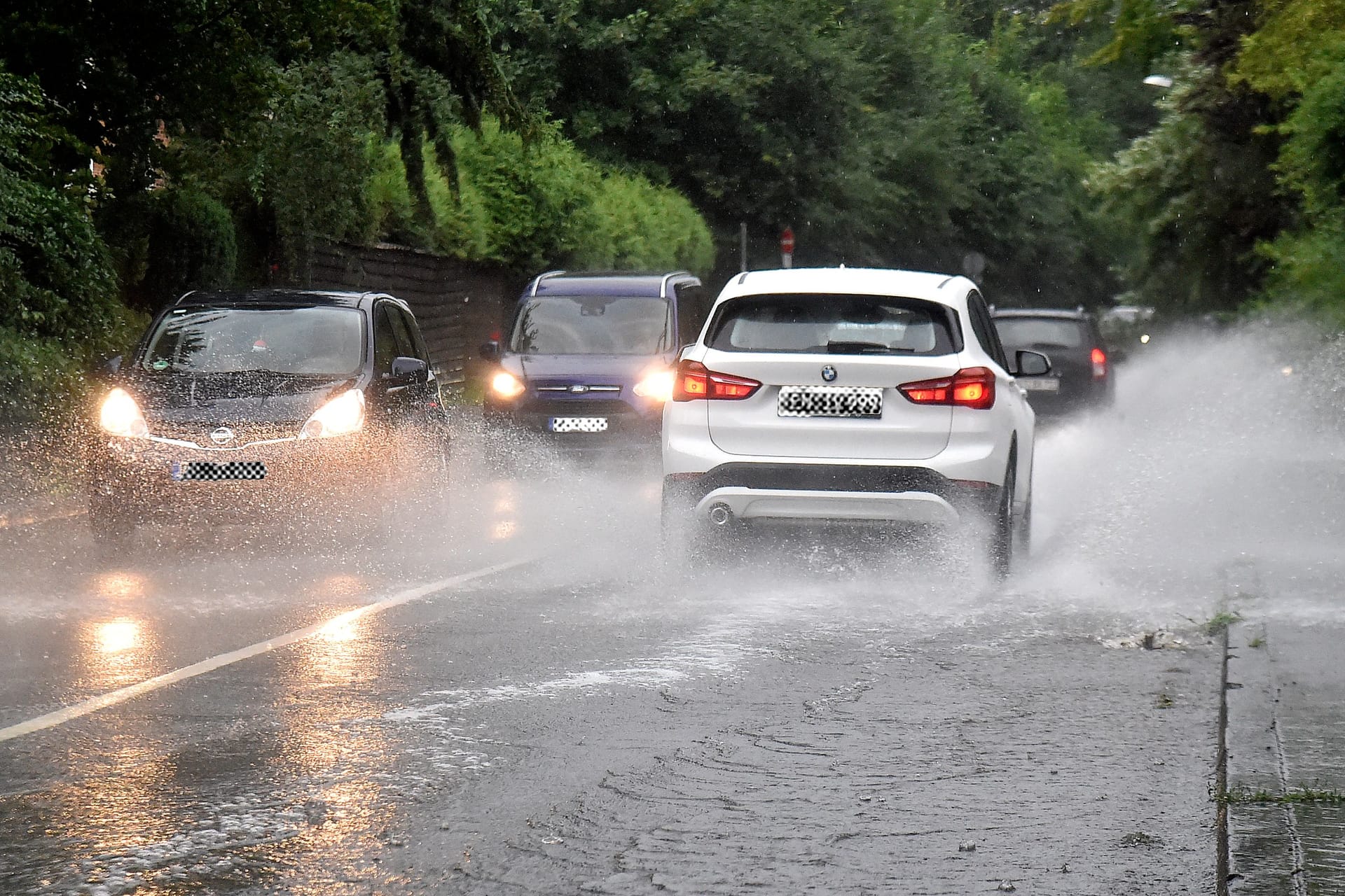 Mehrere Autos fahren über eine überflutete Straße: In Köln und weiten Teilen Nordrhein-Westfalens rechnet der Deutsche Wetterdienst (DWD) ab Sonntag mit Starkregen.