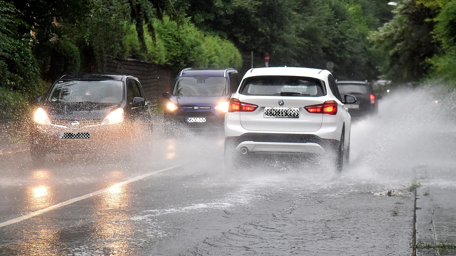 Mehrere Autos fahren über eine überflutete Straße: In Köln und weiten Teilen Nordrhein-Westfalens rechnet der Deutsche Wetterdienst (DWD) ab Sonntag mit Starkregen.