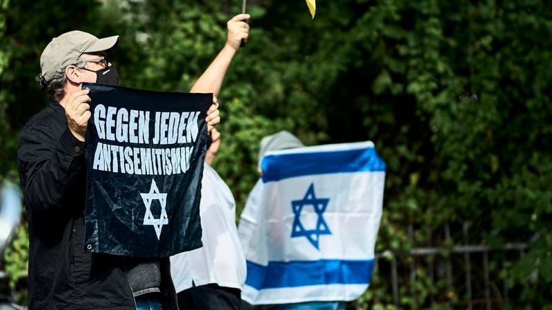 "Gegen jeden Antisemitismus" ist auf dem Transparent zu lesen, das ein Mann am Rande der Internationalist Queer Pride for Liberation (IQP) hält, daneben ist eine israelische Fahne zu sehen.