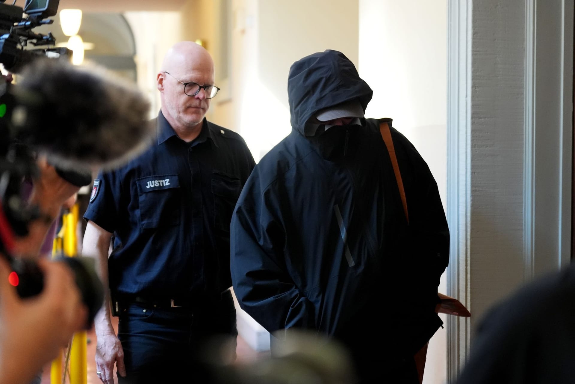 Wer verbirgt sich dahinter? Ein Angeklagter wird von einem Polizisten zum Gerichtssaal begleitet.