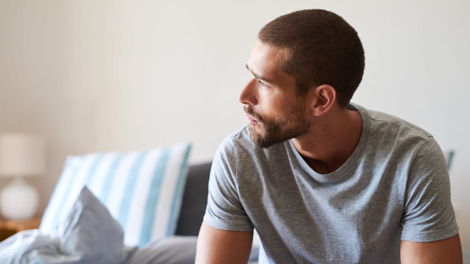 Mann mit nachdenklichem Blick sitzt auf dem Bett: Eine Trichomonaden-Infektion bleibt nicht selten symptomlos.