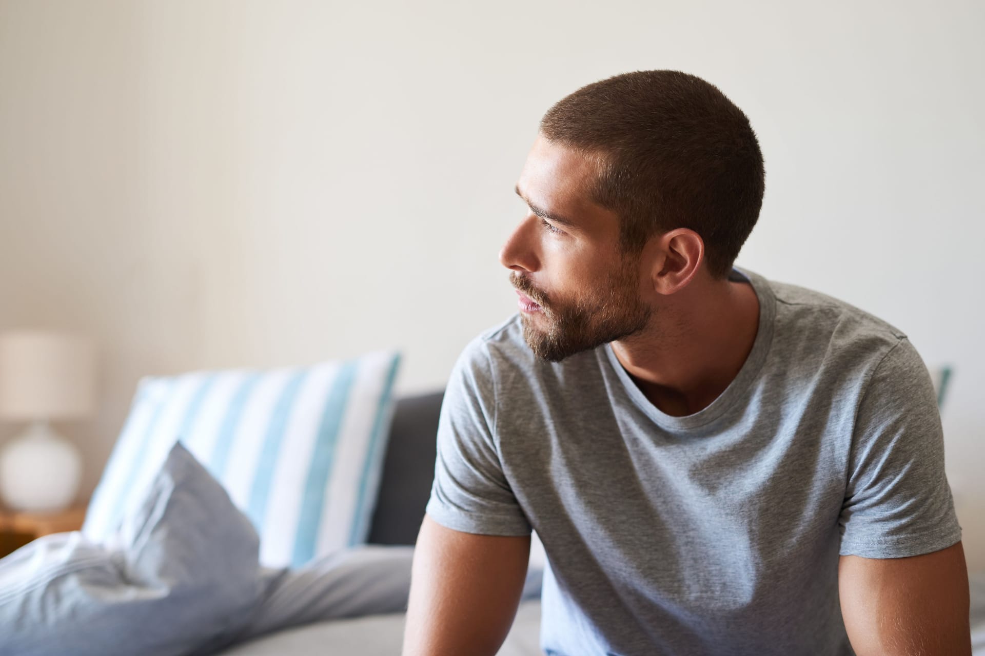 Mann mit nachdenklichem Blick sitzt auf dem Bett: Eine Trichomonaden-Infektion bleibt nicht selten symptomlos.