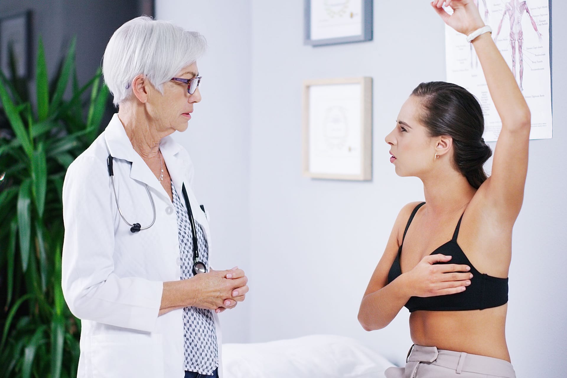 Junge Patientin mit Beschwerde in der Brust bei einer Ärztin: Wie sich die Brust am besten untersuchen lässt, kann die Frauenärztin oder der Frauenarzt erklären.
