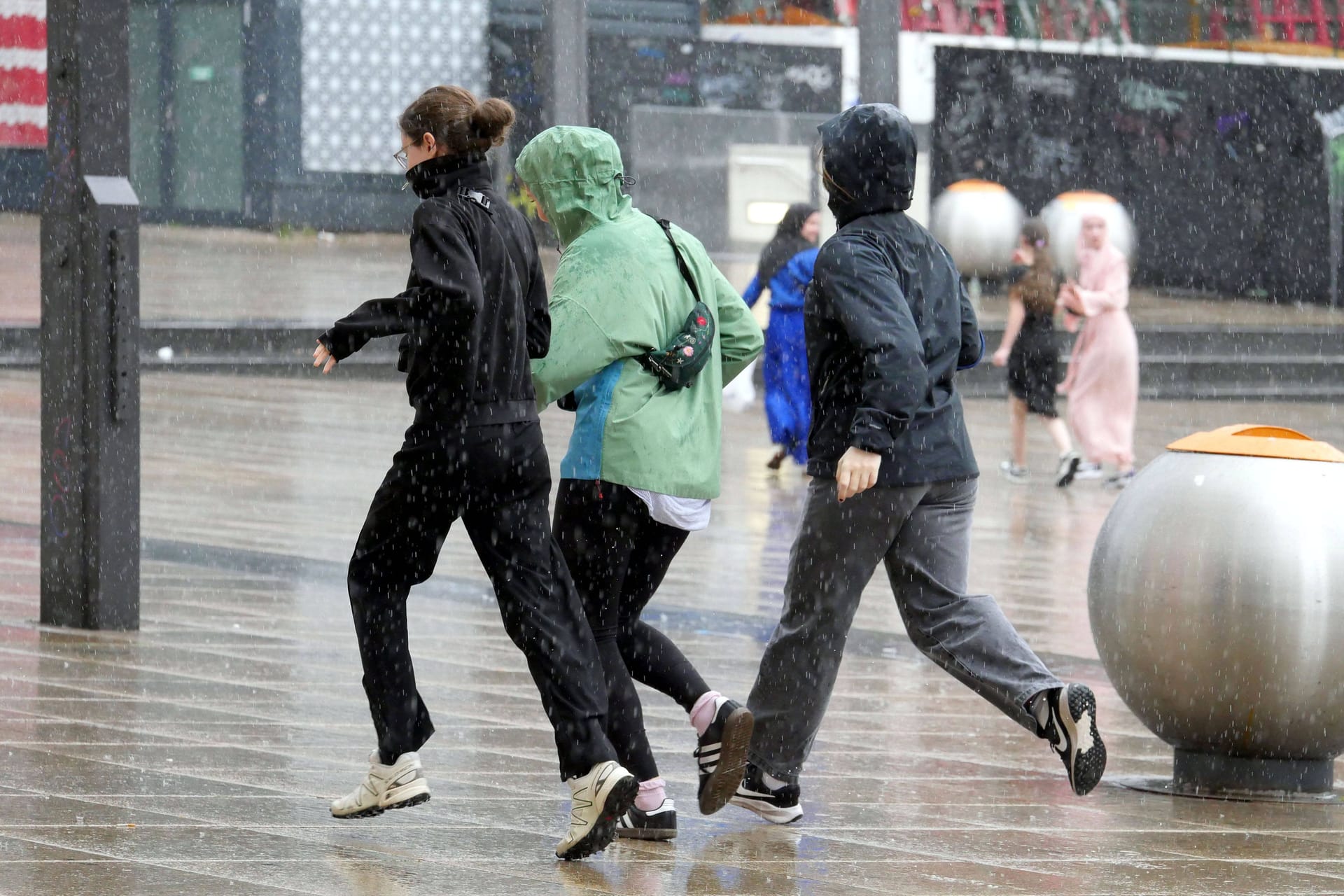 Menschen versuchen sich vor Starkregen in Sicherheit zu bringen (Symbolbild): In Rostock bedroht ein volllaufendes Rückhaltebecken ein Wohngebiet.