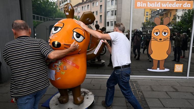 Mitarbeiter des Westdeutschen Rundfunks (WDR) schieben die etwa 75 Kg schwere Fiberglasskulptur der WDR-Maus zum Senderhaus: Die orangefarbene Maus-Figur wurde bei einem Brandanschlag beschädigt und wird nun laut Sender zur "Kur" gebracht. Mitarbeiter des Westdeutschen Rundfunks (WDR) schieben die etwa 75 Kg schwere Fiberglasskulptur der WDR-Maus zum Senderhaus: Die orangefarbene Maus-Figur wurde bei einem Brandanschlag beschädigt und wird nun laut Sender zur "Kur" gebracht.