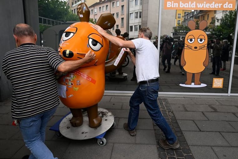 Mitarbeiter des Westdeutschen Rundfunks (WDR) schieben die etwa 75 Kg schwere Fiberglasskulptur der WDR-Maus zum Senderhaus: Die orangefarbene Maus-Figur wurde bei einem Brandanschlag beschädigt und wird nun laut Sender zur "Kur" gebracht.