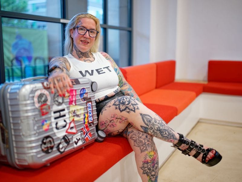 "Mimi", Teilnehmerin einer FKK-Swinger-Reise, sitzt kurz vor der Abreise ins französische Cap d’Agde mit ihrem Koffer im Mannheimer Rathaus.