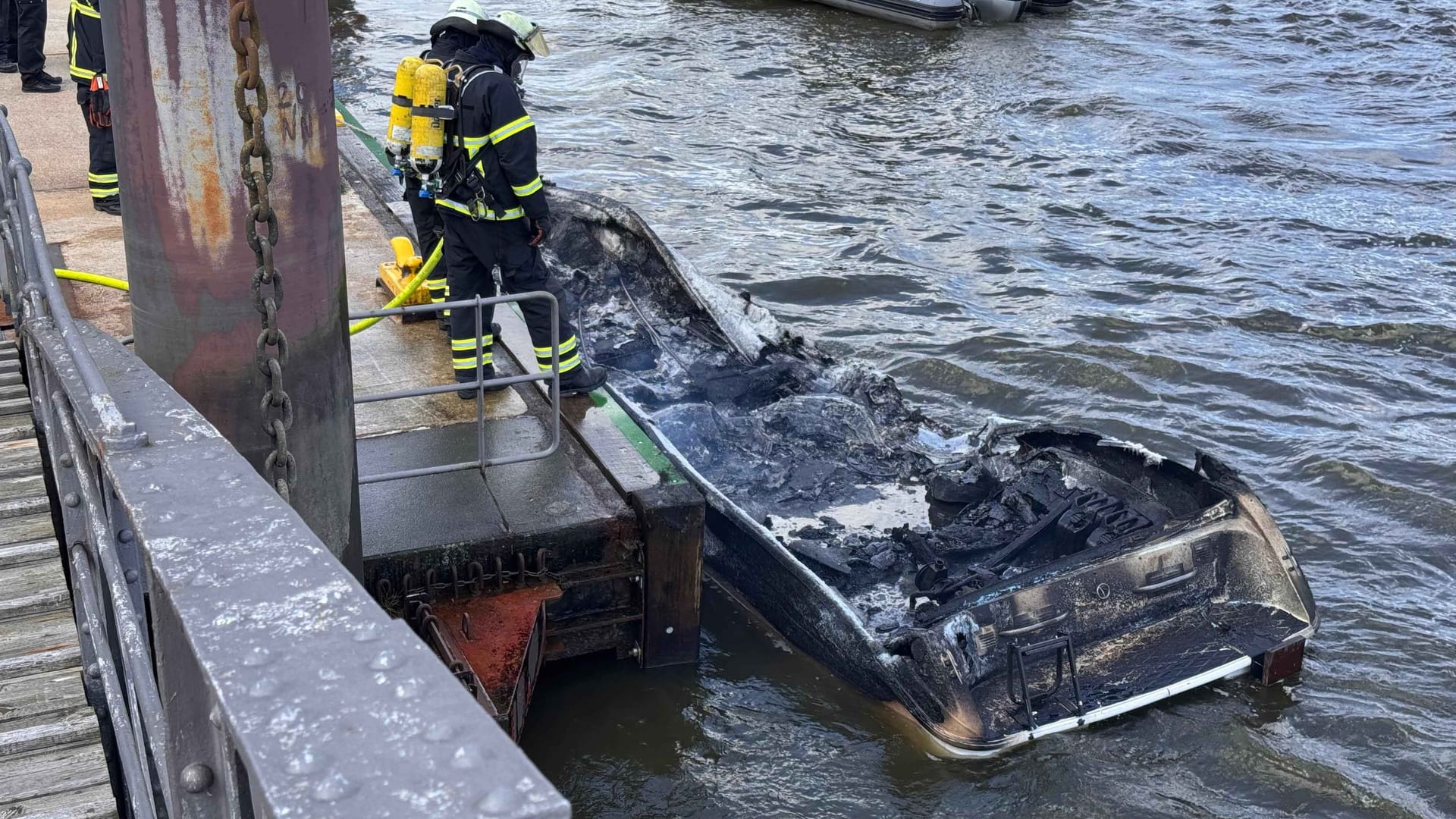 Feuerwehrleute sichern das völlig verkohlte Sportboot: Eine Familie war damit am Sonntag auf der Elbe unterwegs.