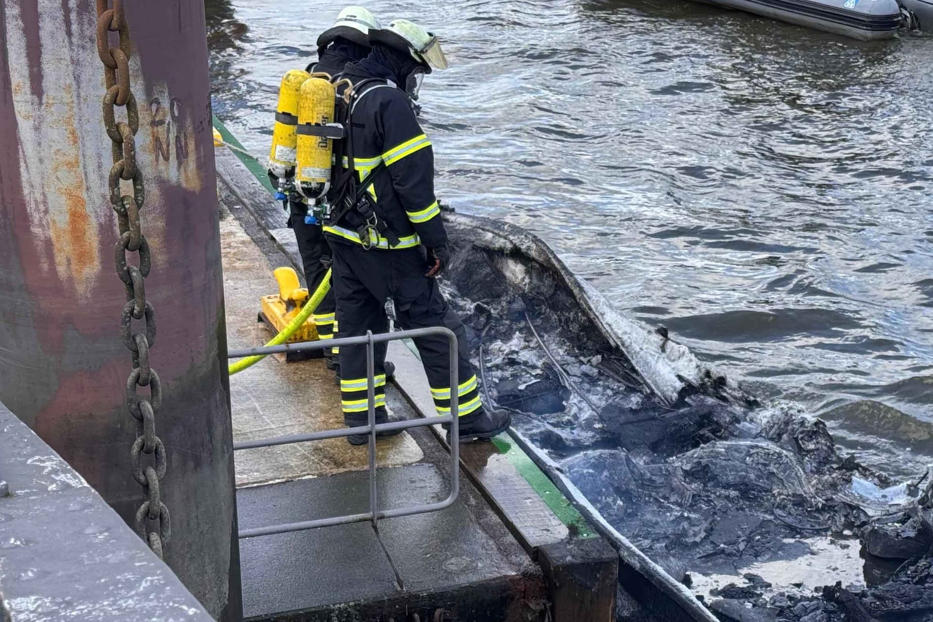 Feuerwehrleute sichern das völlig verkohlte Sportboot: Eine Familie war damit am Sonntag auf der Elbe unterwegs.