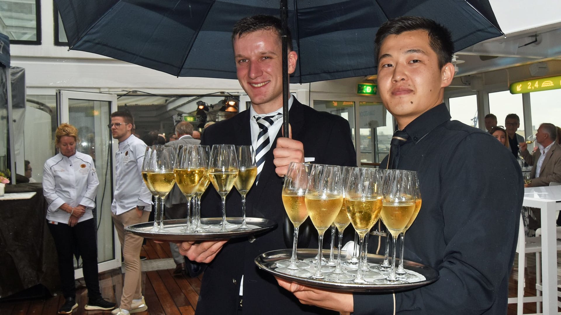 Auch bei Hamburger Schietwetter muss der Champagner serviert werden: Die beiden Kellner an Deck 8 helfen sich mit einem Regenschirm aus.