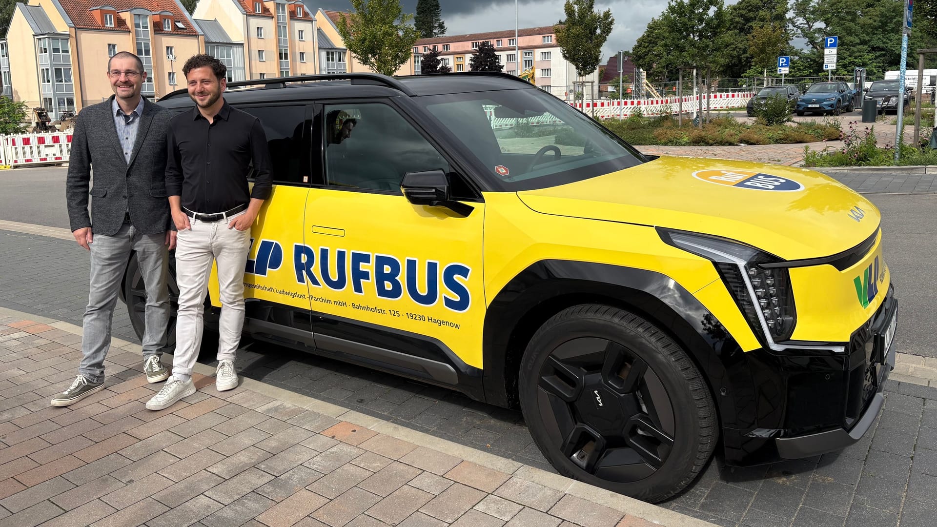 Grünen-Chef Felix Banaszak und der Geschäftsführer der Verkehrsgesellschaft Ludwigslust Parchim, Stefan Lösel, posieren am 01.08.2025 vor einem Rufbus am Hauptbahnhof in Ludwigslust.