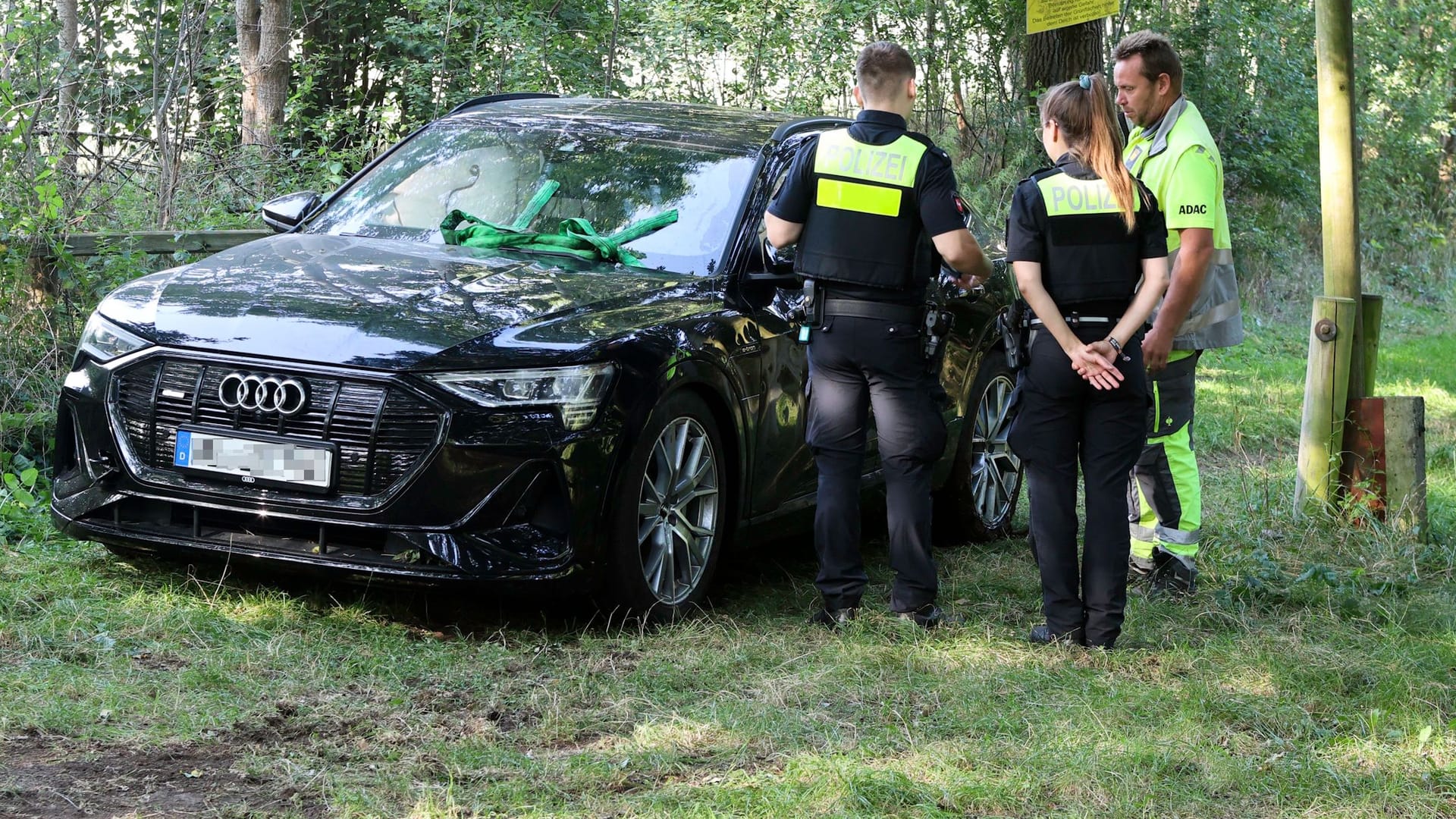 Polizei und ADAC stehen neben dem in die Wümme gestürzten Audi: Der Fahrer des Elektroautos saß offenbar betrunken am Steuer.